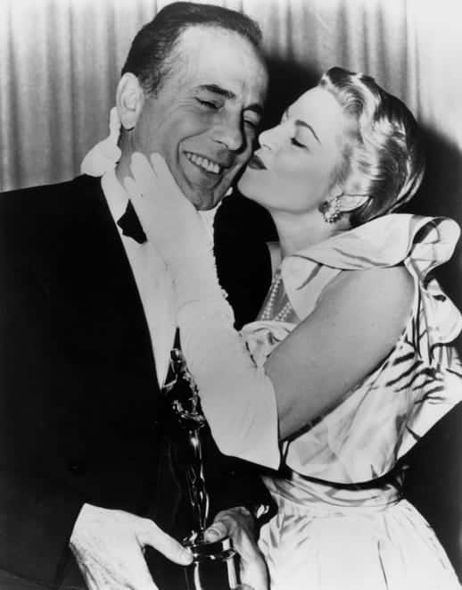 Humphrey Bogart receives a kiss from Claire Trevor while posing backstage with the best actor Oscar he won for his role in "The African Queen" in 1952.